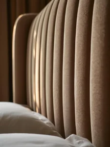 A close-up detail shot of a bespoke channel-tufted upholstered bed headboard