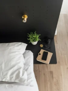 A close-up of a matte black powder-coated steel pegboard accent wall beside a bed