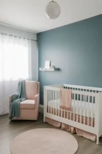 a girl nursery with a matte dusty blue accent wall behind a white crib with a blush linen skirt