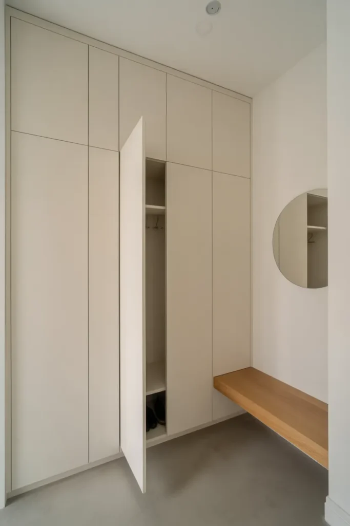 A hyper-minimal mudroom with full-height flush white cabinetry covering an entire wall