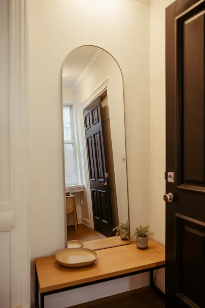 A very tall, slim arched mirror with a thin matte black frame leans against the wall